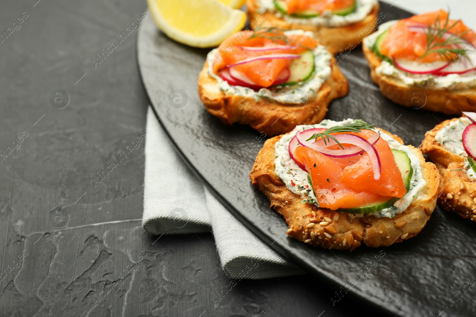 Photo of Tasty canapes with salmon, cucumber, radish and cream cheese on black table, space for text