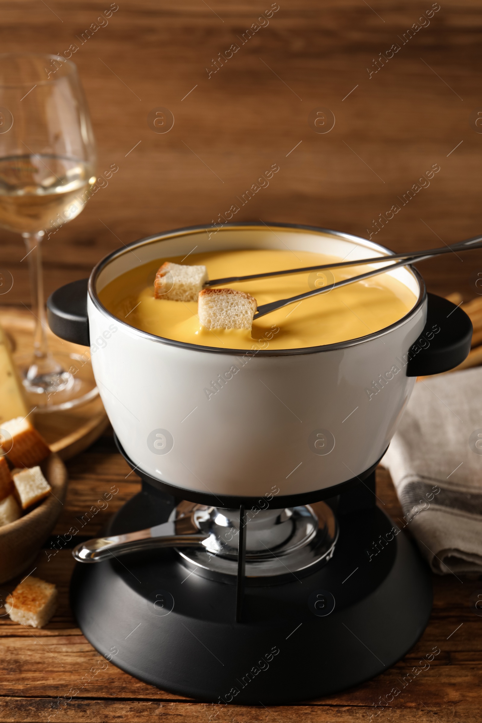 Photo of Pot of tasty cheese fondue and forks with bread pieces on wooden table