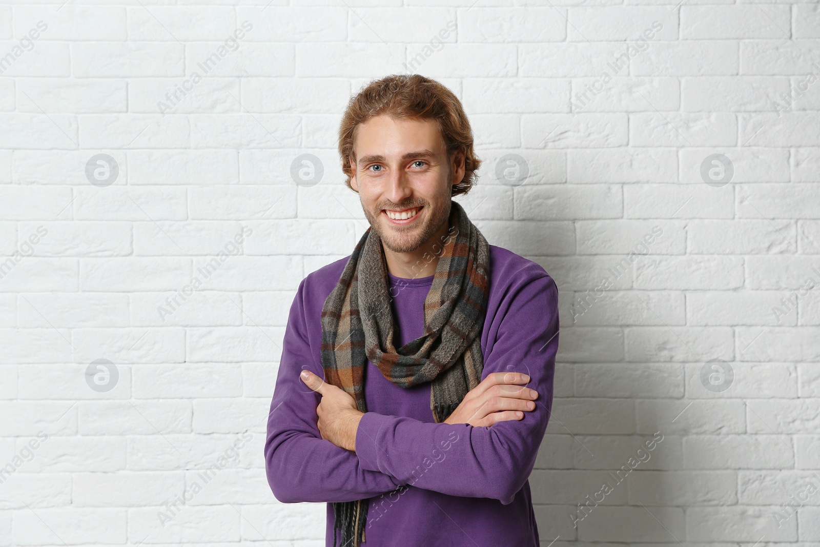 Photo of Handsome young man in warm sweater with scarf near white brick wall