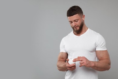 Photo of Handsome man applying body cream on light grey background, space for text