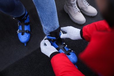 Image of Young man helping his girlfriend to put on ice skates outdoors, above view