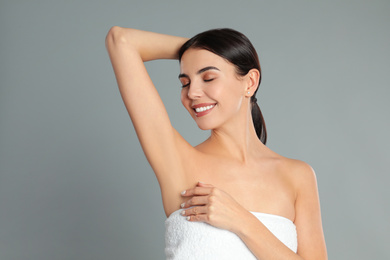 Young woman showing hairless armpit after epilation procedure on grey background