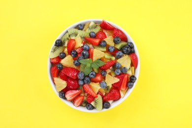 Photo of Yummy fruit salad in bowl on yellow background, top view