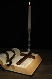 Photo of Church candle, Bible, rosary beads and cross on wooden table against black background