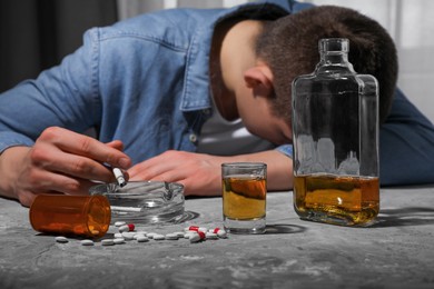 Photo of Alcohol and drug addiction. Man with smoldering cigarettes, whiskey and pills at grey textured table, selective focus