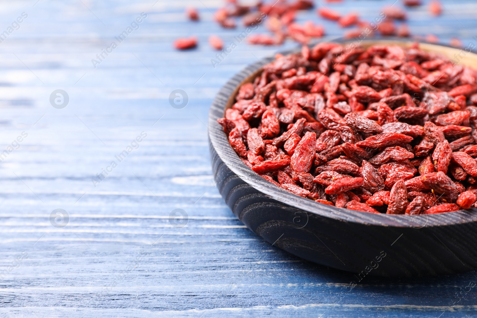 Photo of Dried goji berries on blue wooden table, closeup