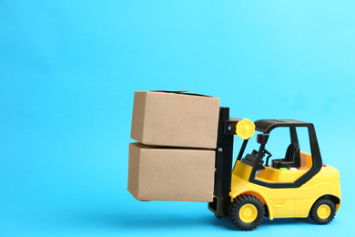 Photo of Forklift model and carton boxes on light blue background. Courier service