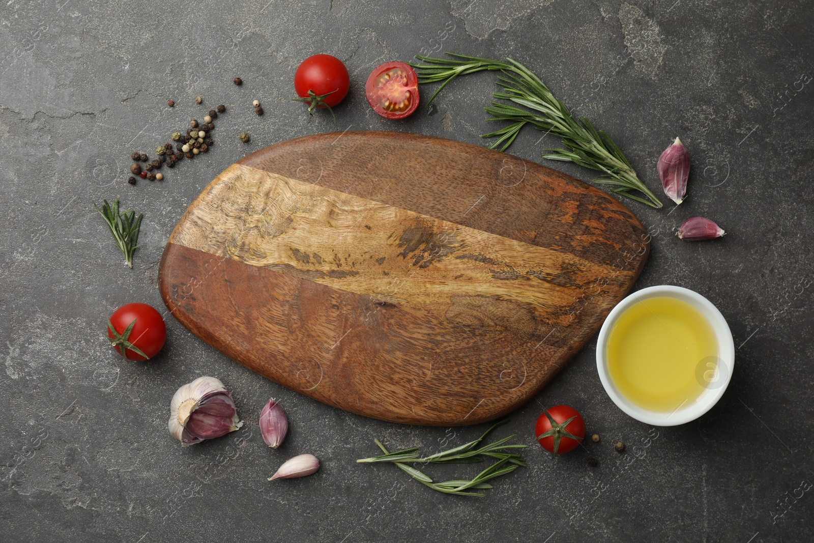 Photo of Cutting board, rosemary, garlic, oil and tomatoes on black table, flat lay. Space for text