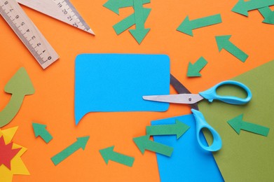 Photo of Scissors and different paper figures on orange background, flat lay. Space for text