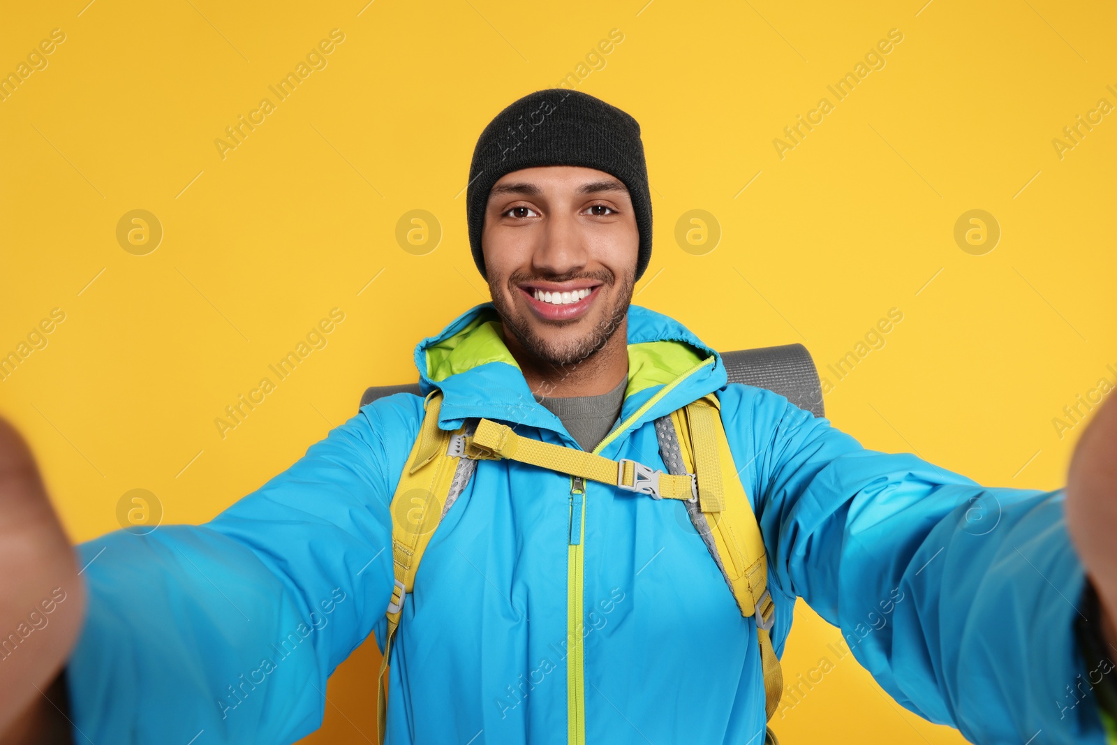 Photo of Happy tourist with backpack taking selfie on yellow background