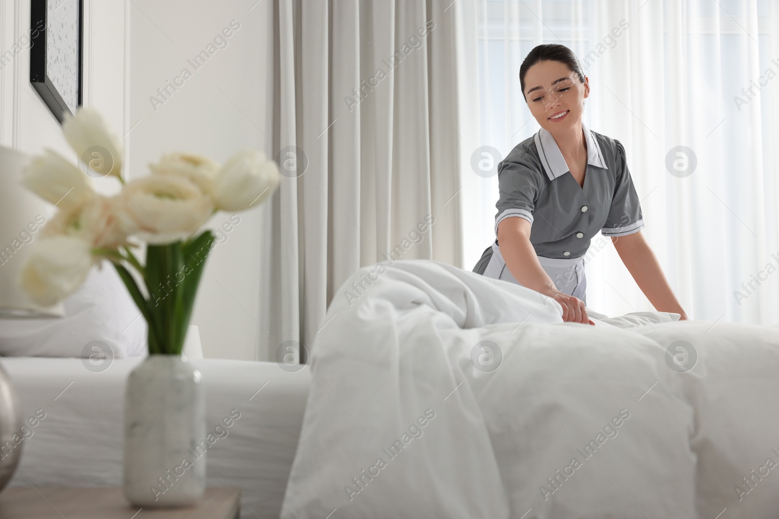 Photo of Young chambermaid making bed in hotel room. Space for text
