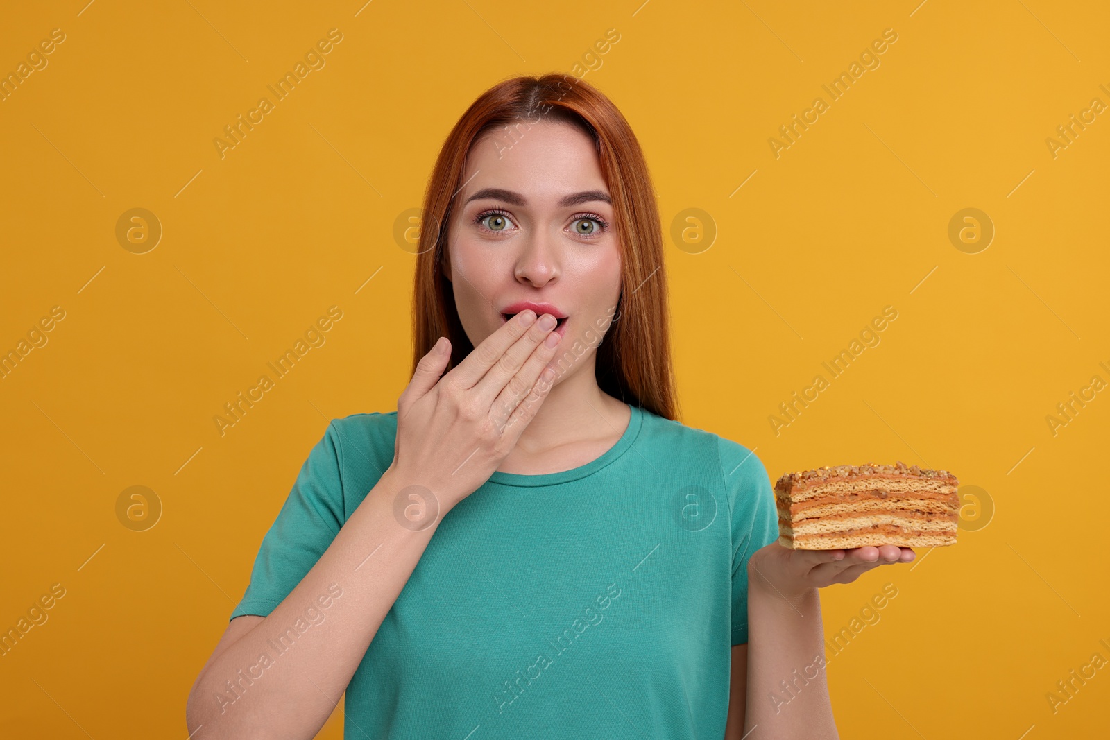 Photo of Emotional young woman eating piece of tasty cake on orange background
