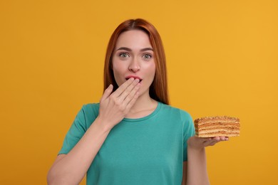 Photo of Emotional young woman eating piece of tasty cake on orange background
