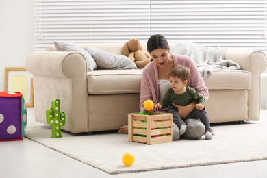 Young nanny and cute little baby playing with toys at home