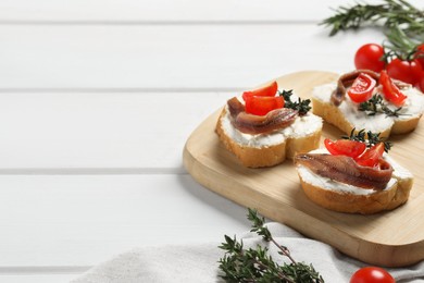 Delicious sandwiches with cream cheese, anchovies and tomatoes on white wooden table, space for text