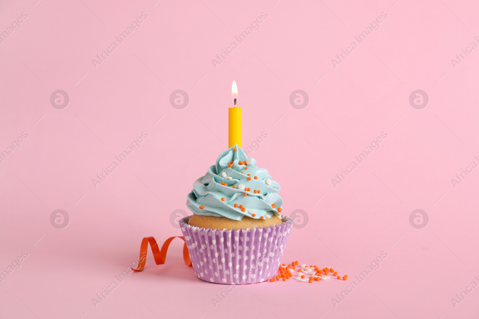 Photo of Birthday cupcake with burning candle, streamer and sprinkles on pink background