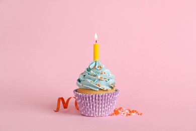 Birthday cupcake with burning candle, streamer and sprinkles on pink background