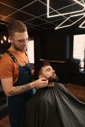 Photo of Professional hairdresser working with bearded client in barbershop