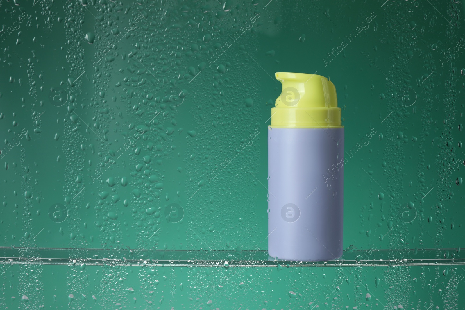 Photo of Bottle with moisturizing cream on green background, view through wet glass. Space for text