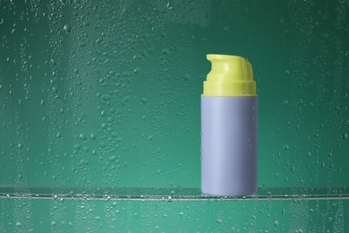 Photo of Bottle with moisturizing cream on green background, view through wet glass. Space for text