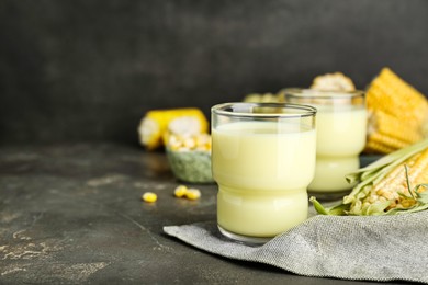 Tasty fresh corn milk in glasses and cobs on grey table. Space for text