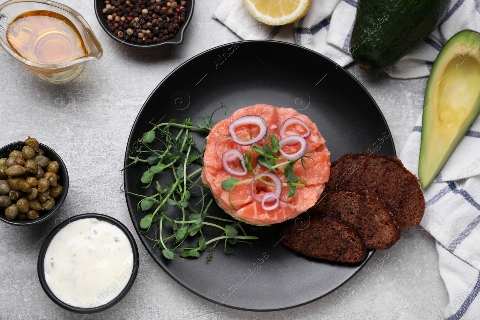 Photo of Tasty salmon tartare with avocado, microgreens and croutons on grey table, flat lay