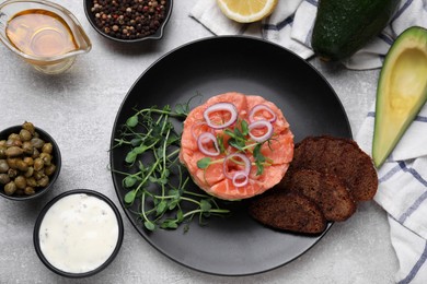 Tasty salmon tartare with avocado, microgreens and croutons on grey table, flat lay