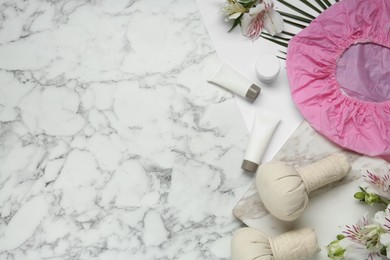 Photo of Flat lay composition with shower cap and toiletries on white marble background. Space for text