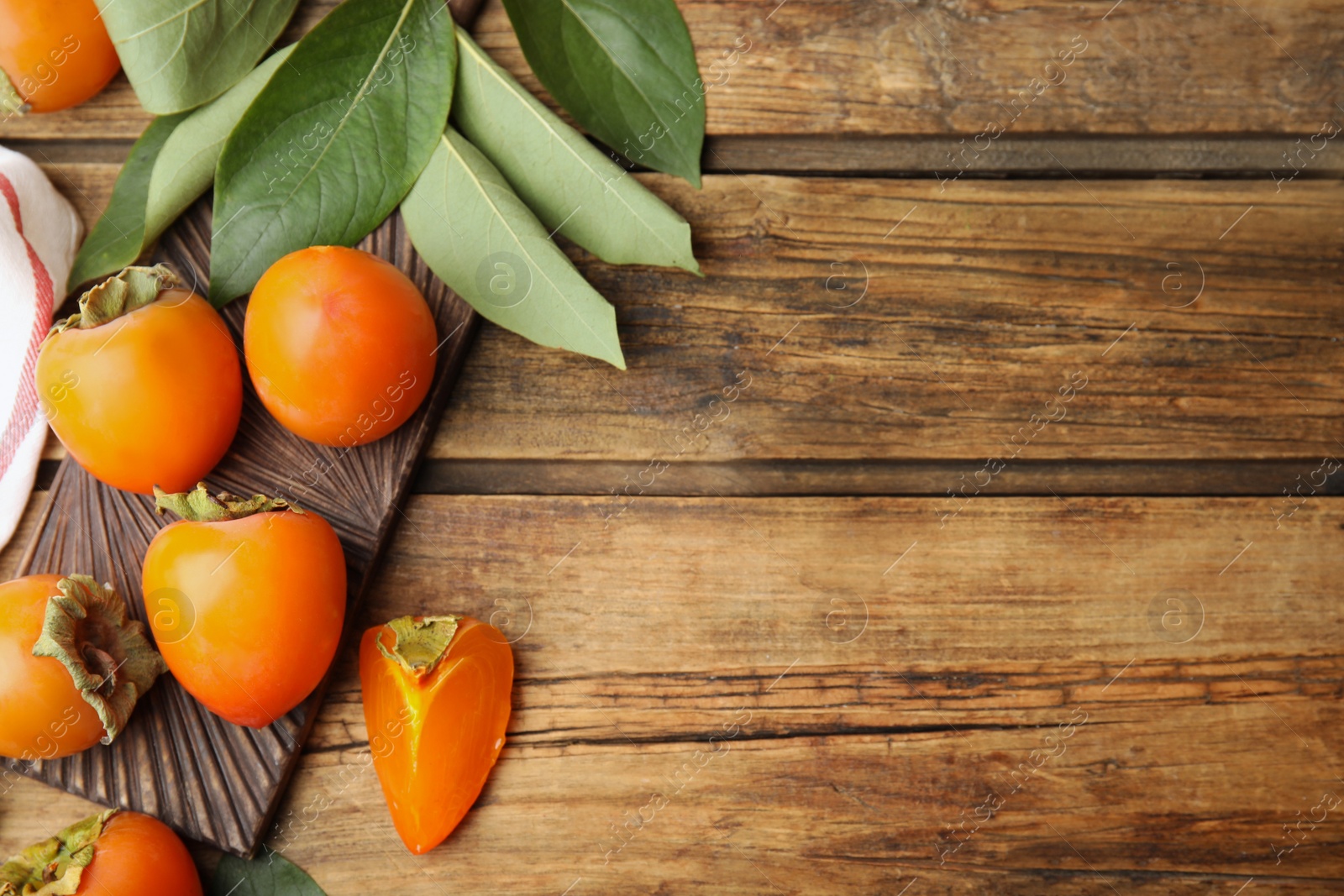 Photo of Delicious fresh persimmons and green leaves on wooden table, flat lay. Space for text