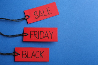 Red tags with words BLACK FRIDAY SALE on blue background, flat lay. Space for text