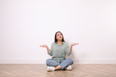 Photo of Young woman sitting on floor near white wall indoors