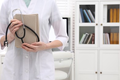 Photo of Doctor holding books and stethoscope indoors, closeup with space for text. Medical education
