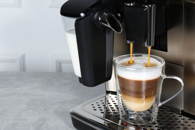 Photo of Modern coffee machine making latte into glass cup on grey table, closeup. Space for text