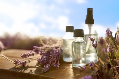 Photo of Bottles of lavender essential oil on wooden table in field. Space for text