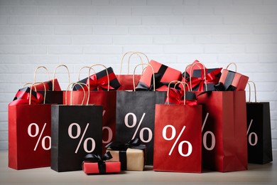 Image of Discount offer. Many shopping bags with percent signs and gift boxes against white brick wall
