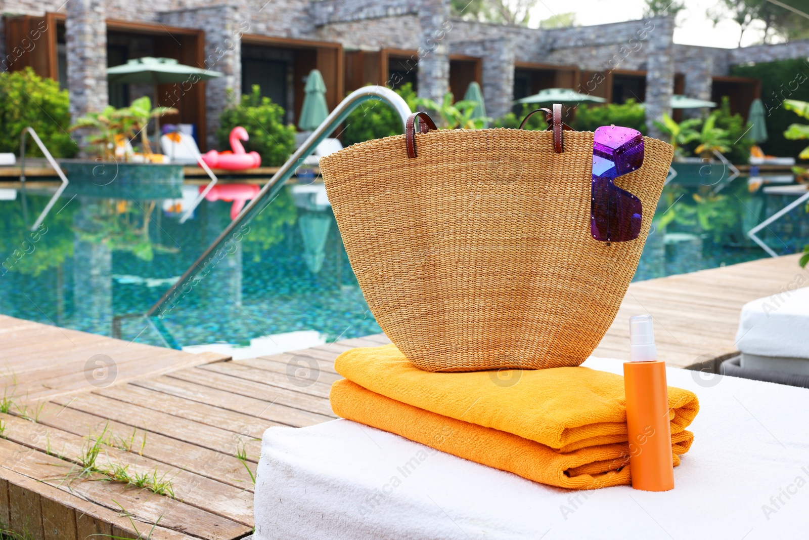Photo of Wicker bag with beach accessories on sunbed near outdoor swimming pool. Luxury resort