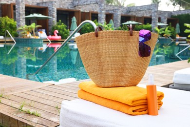 Photo of Wicker bag with beach accessories on sunbed near outdoor swimming pool. Luxury resort