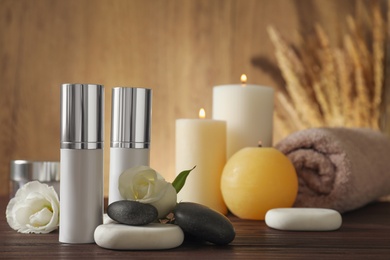 Composition with cosmetic products, spa stones and burning candles on wooden table