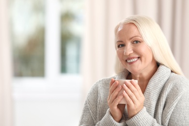 Portrait of beautiful older woman with cup of tea against blurred background. Space for text