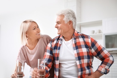 Photo of Affectionate senior couple with glasses of water in kitchen