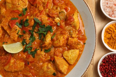 Delicious chicken curry and spices on wooden table, flat lay