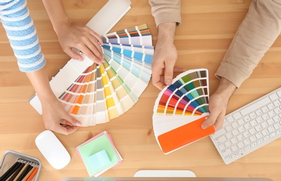 Photo of Designers with paint color palette samples at table, top view
