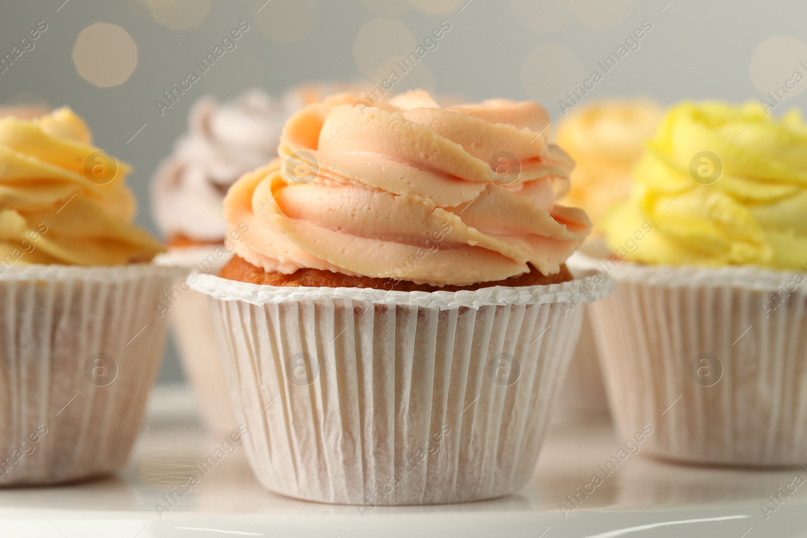 Photo of Tasty cupcakes on white table against blurred lights, closeup