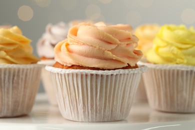 Photo of Tasty cupcakes on white table against blurred lights, closeup
