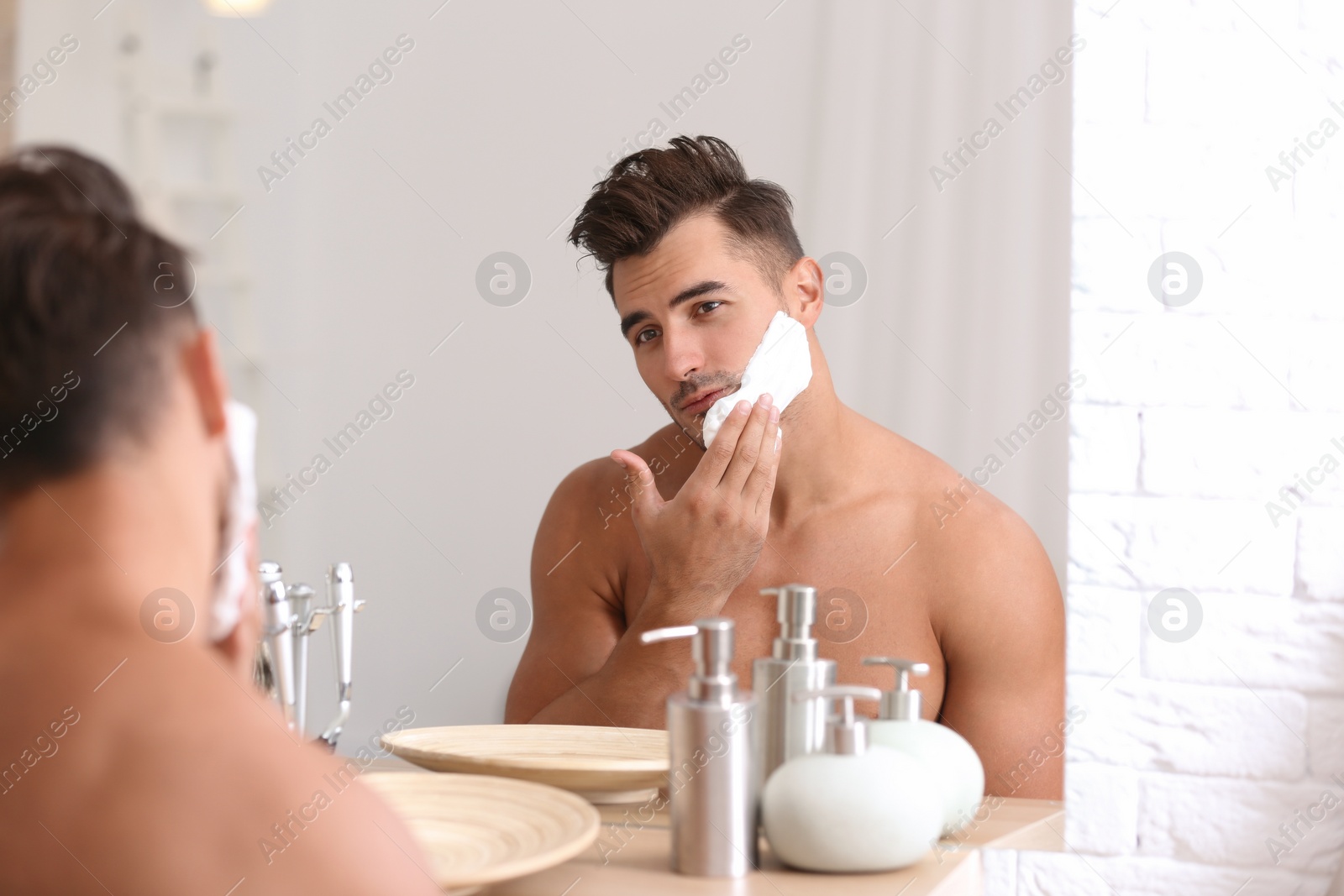 Photo of Young man applying shaving foam near mirror in bathroom