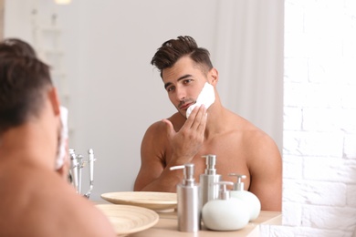 Photo of Young man applying shaving foam near mirror in bathroom