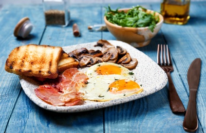 Plate with fried eggs, bacon, mushrooms and toasts on wooden background