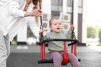 Photo of Nanny and cute little boy on swing outdoors
