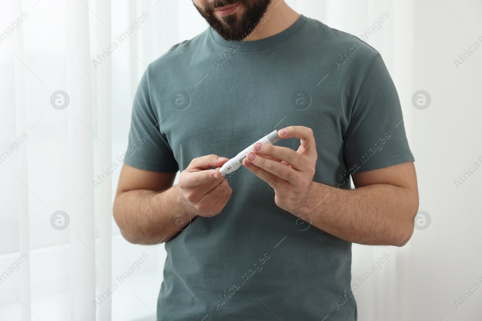 Photo of Diabetes test. Man checking blood sugar level with lancet pen at home, closeup