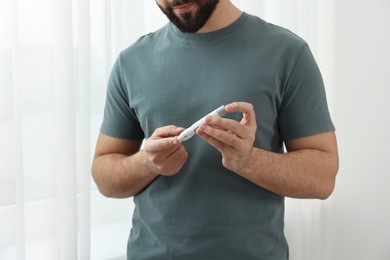 Diabetes test. Man checking blood sugar level with lancet pen at home, closeup